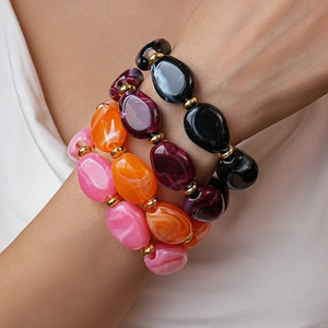 Stacked acrylic pebble bracelets with marble texture and gold beads on a wrist