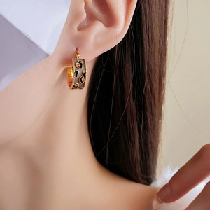 Close-up of vintage C-shape gold-plated earrings with enamel heart patterns on model