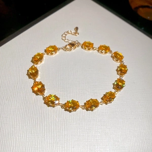 Detail of gold bracelet featuring oval yellow gemstones with heart charm extension chain