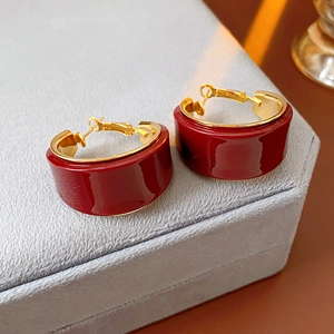 Close-up of gold-plated C-shaped earrings with burgundy resin on a gray velvet stand