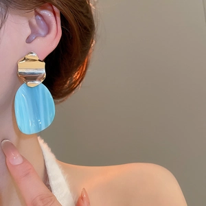 Close-up of woman wearing gold wavy earrings with blue marble textured resin pendants