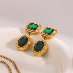 Detail of vintage gold earrings with emerald green stones on white plate background