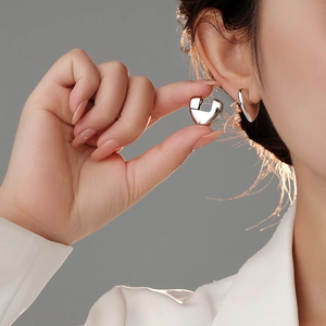 Polished silver 3D heart earrings shown in a close-up lifestyle shot for women