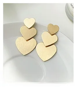 Close-up of triple layered matte gold heart drop earrings on a white ceramic plate