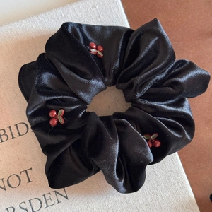 Detail of a black velvet hair ring featuring red cherry accents on a minimalist book background