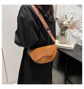 Detail of brown PU leather saddle bag featuring a wide patterned woven shoulder strap