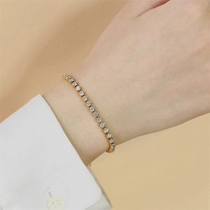 Detail of a gold tennis bracelet featuring sparkling round-cut crystals on a model's wrist
