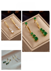 Close-up of gold snake chain earrings with square green and white zircon crystals