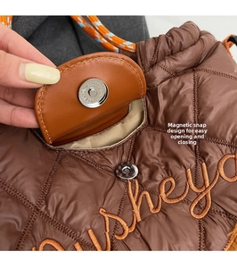 Detail of magnetic buckle on brown quilted tote with orange embroidery and woven handle