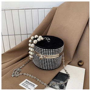 Detail of a black velvet cylinder bag featuring sparkling rhinestones and metal bead handle