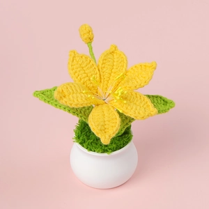 Detail of handmade crochet yellow iris flower in a white ceramic pot with green leaves