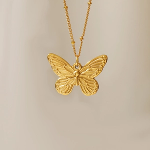 Detail of vintage 18K gold plated butterfly coin pendant with embossed texture on chain