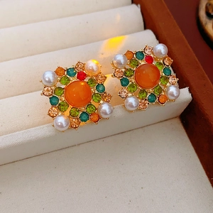 Détail de boucles d'oreilles vintage en or avec gemme orange, strass colorés et perles