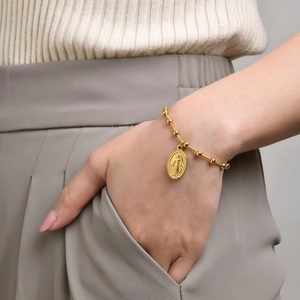 Gold beaded rosary bracelet with oval Virgin Mary pendant worn on wrist for religious style