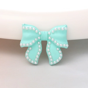 Macro detail of a light blue bow charm with inlaid white pearls for DIY jewelry crafts