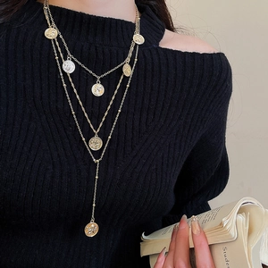 Close-up of layered vintage gold coin pendant necklace styled on a black sweater