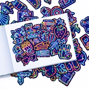 Close-up of holographic neon stickers with cat and gaming motifs on a white notebook