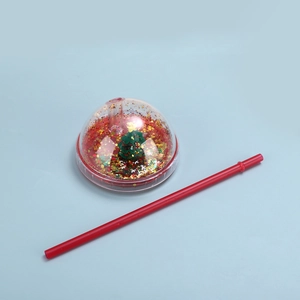 Detail of Christmas dome lid with floating glitter and miniature tree and a red straw