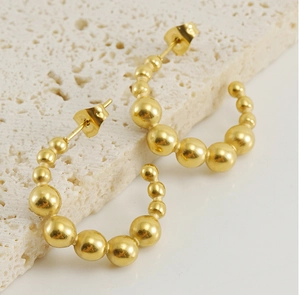 Macro shot of 18K gold beaded C-shape earrings on beige coral stone background