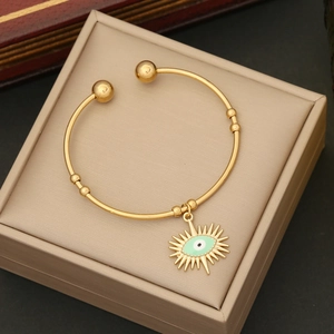 Close-up of golden evil eye sun pendant on a stainless steel bangle over a beige box