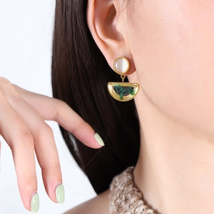 Golden earrings with white round studs and marble-patterned resin charms on model