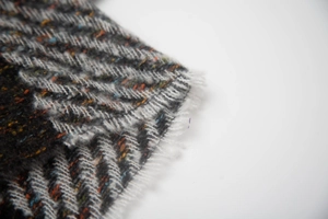 Macro shot of herringbone knit fabric texture with colorful flecks and soft fringe