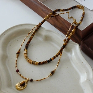 Detail shot of a layered beaded necklace with a golden teardrop pendant on a ceramic tray