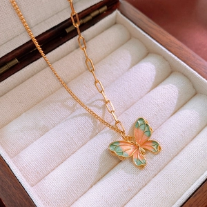 Close-up of pink and green butterfly pendant with gold chain in a jewelry box