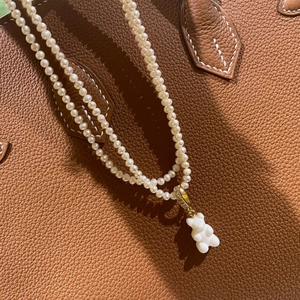 Detail of white gummy bear pendant on double-layer pearl necklace with gold accents