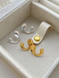 Macro shot of liquid-form C-shape earrings in gold and silver finish on velvet box