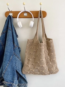 Khaki knitted tote bag with woven texture hanging next to denim jacket on white wall