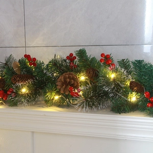 Christmas rattan garland with pine cones, red berries and warm LED lights on marble surface