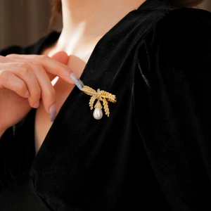 Détail d'une broche épi de blé dorée avec perles et cristaux sur une robe noire chic