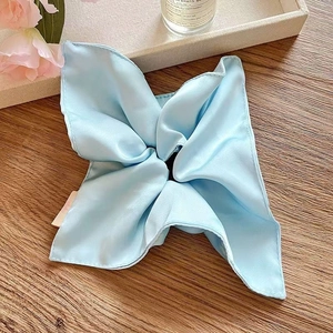 Macro detail of a light blue silk scrunchie scarf with a smooth satin texture on wood