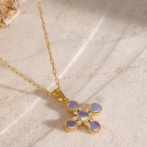 Detailed shot of golden cross necklace with moonstone pendants on a natural stone surface