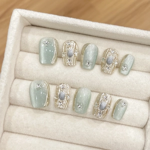 Detailed view of light green press-on nails with cat-eye effect and gold relief patterns