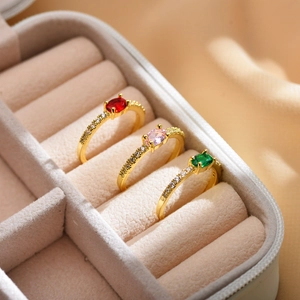 Three elegant gold-plated rings with oval red, pink and green zircon stones in a jewelry box