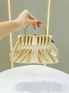 Detail of the golden pleated clutch featuring a round metal handle and spheres clasp