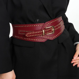 Close-up of wine red elastic waist belt with gold studs and square buckle on black blazer