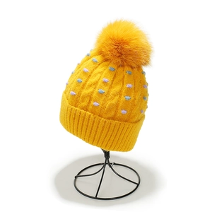 Detalle de gorro de punto amarillo con pompón, trenzado y puntos de colores