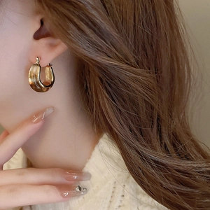 Close-up of model wearing amber resin horseshoe earrings in polished gold finish