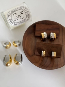 Detailed top view of gold and silver mixed metal drop earrings on a wooden display tray