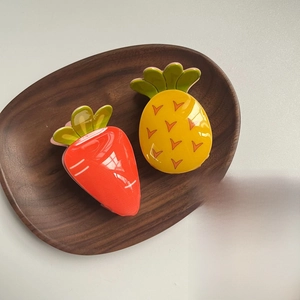 Detail of cute acrylic strawberry and pineapple hair clips on a wooden tray
