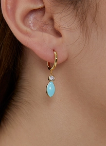Close-up of gold dangle earrings with blue marquise stone and zircon on female ear