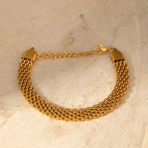 Détail de bracelet à maille dorée avec fermoir mousqueton sur fond en pierre beige