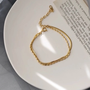 Minimalist 18K gold double-layer snake and beaded chain bracelet displayed in a ceramic tray