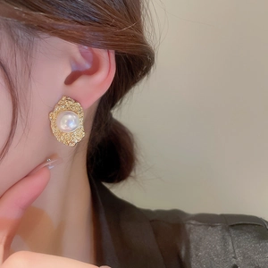 Detailed view of vintage gold textured flower earrings with pearl on a female model