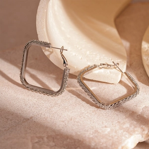 Close-up of square silver hoop earrings with textured edges on natural stone display