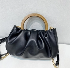 Detail of black pleated cloud bag featuring a unique wooden ring handle and gold metal chain