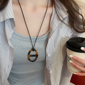 Retro amber pig-nose resin pendant on black rope chain shown on a model with coffee